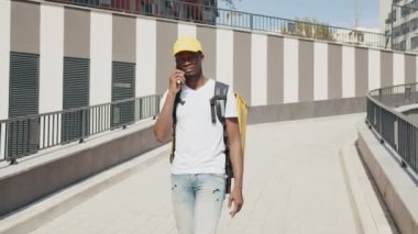 Kurye telefonda konuşur ve emirleri uygular. Çeşitli malların hızlı teslimatı. Genç bir Afrikalı kurye, termal bir sırt çantasıyla bir restorandan ya da dükkandan sipariş getiriyor..