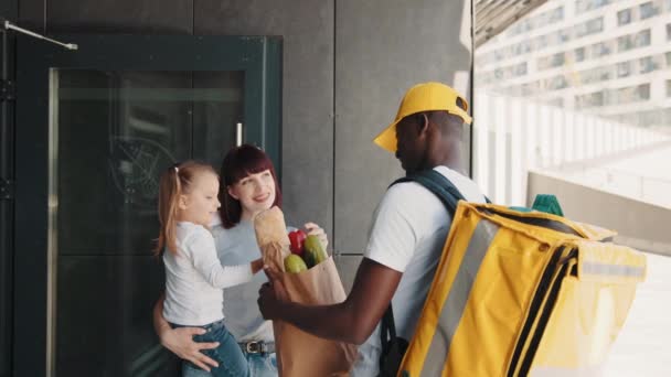 Ekspresowa dostawa wegetariańskiej i zdrowej żywności przez kuriera. Afroamerykańska kurier przynosi paczkę żywności, owoców i warzyw przed domem do pięknej kobiety z dzieckiem — Wideo stockowe
