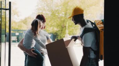 İnternetten e-ticaret mağazaları satın al. Kurye, kız ve annesi için evin kapısına bir paket getiriyor. Paketi açarken, mutlu bir çocuk oyuncak ayıyı kutusundan çıkarır..