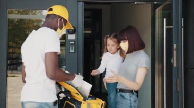 Anne ve kızı bir paket alıyorlar. Eldiven ve maske takan bir kurye, koronavirüs salgını sırasında yiyecek ve malzeme dağıtır. İnternetten alışveriş teslimatı. Koronavirüs salgını sırasındaki teknolojiler.