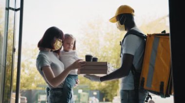 Evinin kapısında bir çocukla gülümseyen güzel bir genç kadın ve ona karton kutu dolusu lezzetli buharda pişmiş pizza veren bir pizzacıyla tanışır. Pizza teslimatçısı.