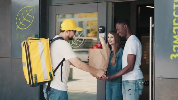 Servizio di consegna di cibo intelligente, l'uomo consegna cibo fresco al destinatario e alla giovane donna, la coppia multirazziale riceve ordini da corriere, consegna espressa, consegna di cibo, concetto di shopping online — Video Stock