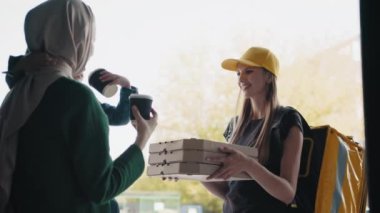 Yemek servisi. Neşeli bir kurye, kutular dolusu pizza ve içecek getiriyor. Müslüman bir kadına ve çocuğuna evinin önünde gülümsüyor ve pizza gösteriyor. Cafe ve Restoran Teslimat Servisi