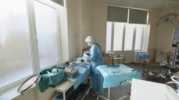 Egy védőmaszkos női egészségügyi dolgozó portréja egy asztalnál, sebészeti eszközökkel. Sebészeti műszer. A sebész egy műszert tart a műtéthez. Műtétre való felkészülés — Stock videók