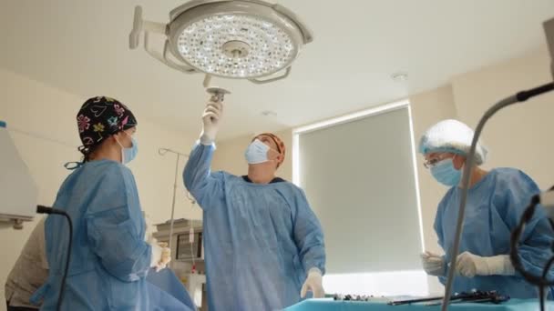 Chirurgische lamp in de operatiekamer, licht, instelling. Professionele chirurgen die Chirurgie Lichten aandoen terwijl ze bukken voor Patiënt. De medische lamp gaat uit en we zien licht en momentum — Stockvideo