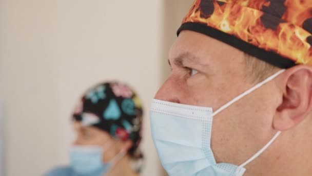 Närbild av manliga läkare bär kirurgmask i operationssalen på sjukhuset. Porträtt av självsäker skicklig glad allmänläkare. Praktikant eller kirurg ler bakom medicinsk mask — Stockvideo