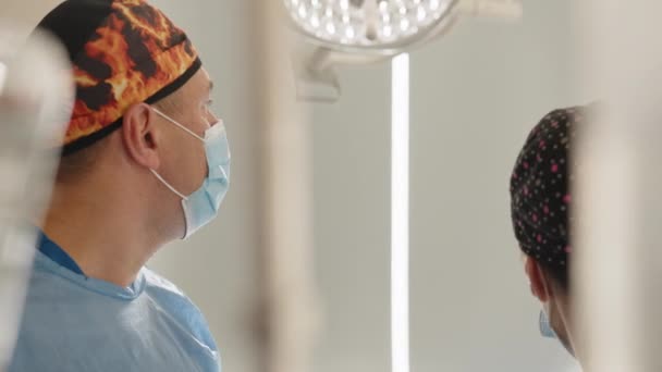 Chirurgo caucasico professionista sanitario maschile in una sala operatoria ospedaliera con cappuccio e maschera chirurgica. Medici e un'infermiera stanno guardando il monitor dell'endoscopio durante l'intervento chirurgico. — Video Stock