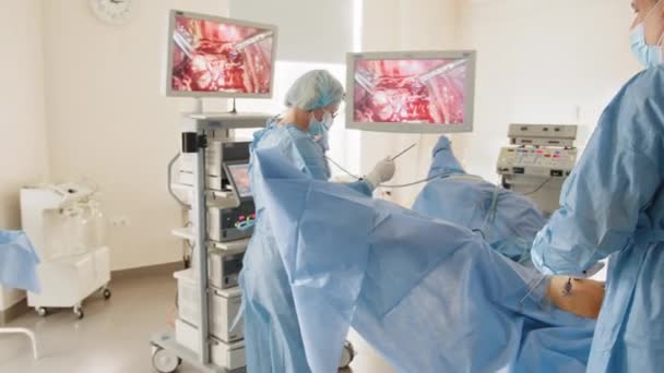 Surgery hospital cancer. Endoscopic Operation. Couple of surgeons stand on both sides of modern equipment. Hands of doctors with metal instruments move under the apparatus dealing with patients body. — Stock Video