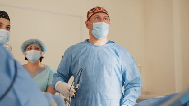 Cirujano durante la cirugía. Retrato de médico en gafas mientras está de pie en quirófano. Hombre cirujano en guantes estériles, uniforme quirúrgico azul y mascarilla protectora, listo para cirugía en clínica. — Vídeo de stock