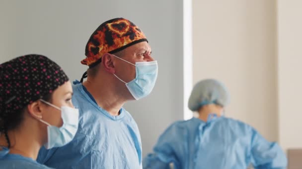 Chirurgien caucasien professionnel de la santé dans un bloc opératoire d'hôpital portant une casquette et un masque chirurgicaux. Professionnels de la chirurgie de soins de santé équipe médecins concept. Chirurgie réussie. Chirurgien masculin — Video