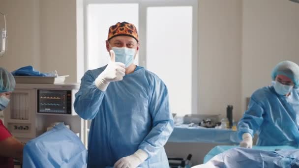 手术成功了快乐的年轻男性专业外科医生与他的医疗团队合作成功后，微笑着竖起大拇指 — 图库视频影像