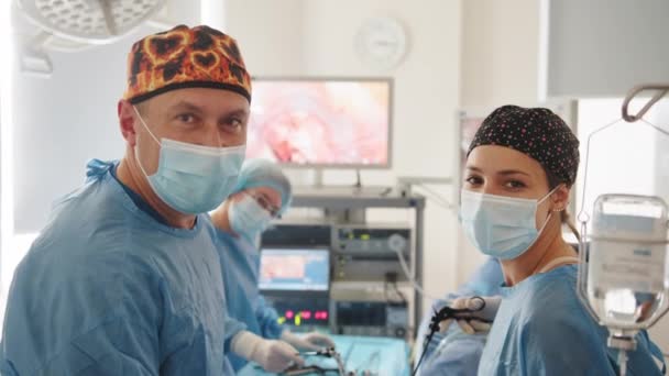 Chirurg se dívá na kameru s kolegy. Týmový chirurg pracuje na operaci v nemocnici. Tým chirurgů pečlivě provádějící operaci s použitím přesných nástrojů v operačním sále — Stock video