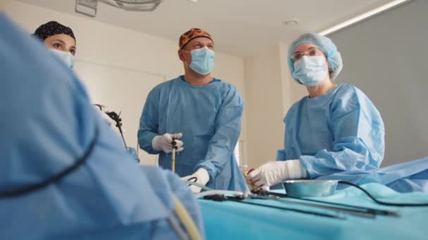 Proceso de cirugía ginecológica utilizando equipo laparoscópico. Grupo de cirujanos en quirófano con equipo quirúrgico. Retrato cintura arriba de enfermeras con máscaras protectoras y guantes estériles — Vídeos de Stock