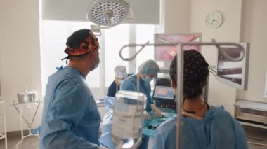 Cerrahların ekibinin arka görüşü, hastane ameliyathanesinde ameliyat öncesi hazırlık yaparken monitörlere, cerrahi laparoskopi aletleriyle çalışan erkek cerrah hastalarına bakıyor. Jinekoloji.