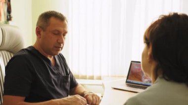 Profesyonel orta yaşlı doktor, hastanedeki bir dolapta masasında otururken iş arkadaşlarıyla konuşuyor. Doktorlar sonuçları tartışıyor. Doktor tanınmayan bir hastayla konuşuyor.