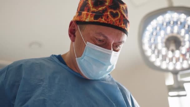Καυκάσιος χειρουργός άντρας επαγγελματίας υγείας σε χειρουργείο νοσοκομείου φορώντας χειρουργικό καπέλο και μάσκα. Χαμηλή γωνία άποψη του Καυκάσιου ανδρός χειρουργός που εκτελεί χειρουργική επέμβαση στο θέατρο. — Αρχείο Βίντεο
