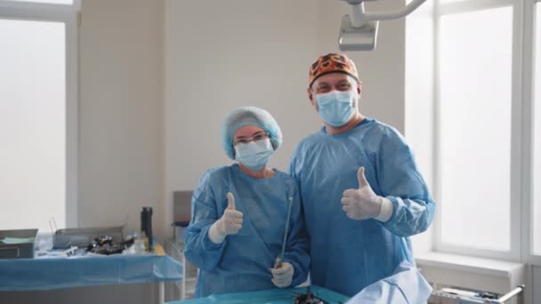 Chirurgia, medycyna i koncepcja ludzi - grupa chirurgów na sali operacyjnej w szpitalu z kciukami w górze. Lekarze w sterylnych rękawiczkach i maskach ochronnych po udanej operacji chirurgicznej. — Wideo stockowe