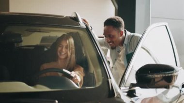 Yetenekli bir Afrikalı satıcı bayan müşteriye galeride yeni lüks bir araba gösteriyor. Beyaz kadın arabada oturuyor ve satın almadan önce tüm detayları kontrol ediyor. Satıcı kadın kadına araba sunar.