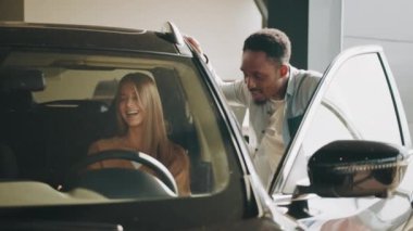 Afro-amerikan delaer yanında durup danışmanlık sağlarken, neşeli beyaz kadın lüks arabanın içinde oturmuş deriyi test ediyor. Otomobil işi kavramı. Satıcı arabası.