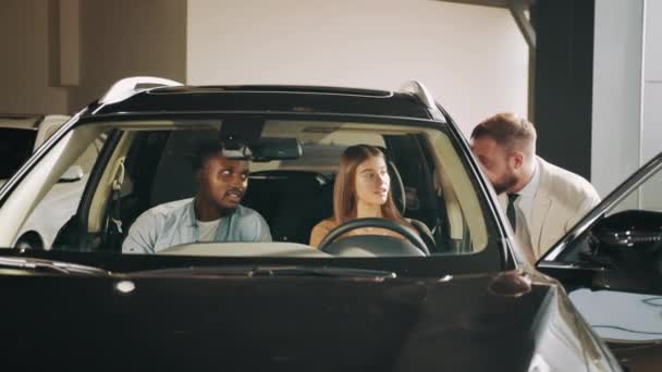 身着正装的汽车经销商在展示室向不同文化的情侣们展示新的豪华汽车模型。非洲裔美国人男子和他的高加索女人参观代理中心选择新的交通工具. — 图库视频影像