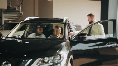Müşteriler arabada oturup iç mekanın tüm detaylarını inceliyor. Satıcı sunar. Erkek ve kadın yeni araç seçiyor. Otomobil işi ve danışmanlık konsepti. Kuaförden araba almak.