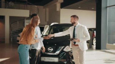 Profesyonel satıcı, modern kuaförde yeni bir arabadan çok kültürlü bir çifte anahtar veriyor. Mutlu Afrikalı adam ve beyaz kadın bayilik merkezinde pahalı şeyler satın alıyorlar. Satıcının verdiği anahtarlar.