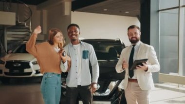 Aşırı neşeli Afrikalı erkek ve beyaz kadın araba satın almaktan duygulandılar. Modern kuaförde ellerinde anahtarlarla bekleyen çok ırklı bir çift. Krupiye anahtar veriyor