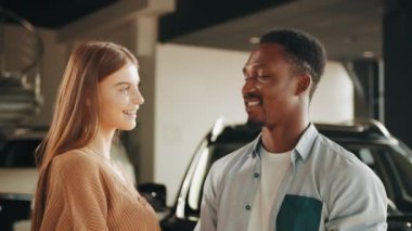 Modern bayilik merkezinde ellerinde anahtarlarla poz veren mutlu çok kültürlü çifti yakın çekim yapın. Afrikalı erkek ve beyaz kadın mutluluklarını araba satın alarak ifade ettikleri için duygusallaşıyorlar..