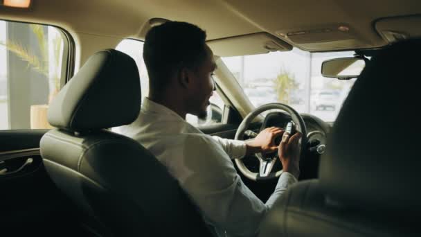 Sorrindo afro homem segurando novas chaves do carro no veículo. Bonito homem parece satisfeito com a compra bem sucedida. Veículo Eco. Motorista aprecia a compra de carro em veículo novo no test drive. Motor de arranque do carro. — Vídeo de Stock