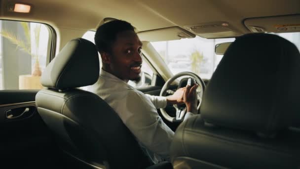 Closeup confiante homem americano africano comprar carro novo. Sorrindo afro homem segurando novas chaves do carro no veículo. Bonito homem parece satisfeito com a compra bem sucedida. Veículo ecológico. — Vídeo de Stock