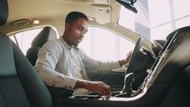 Zijaanzicht van gefocuste Afrikaanse man die op de bestuurdersstoel zit en dashboard gebruikt voor navigatie. Man drukt op touchscreen op auto multimediapaneel, schakelt van radiostation. Een man test een nieuwe auto. — Stockvideo