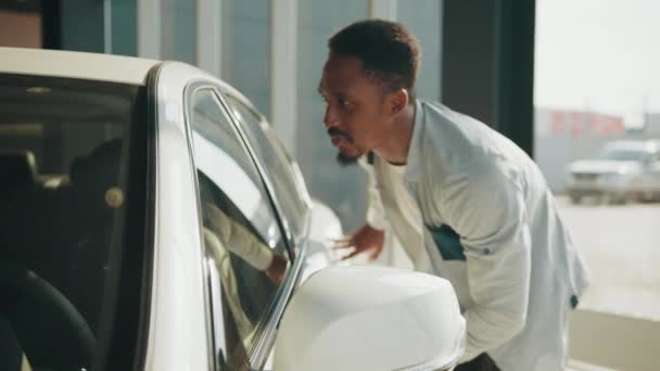 Visitando concesionario de coches. Happy Afro Man tocando nuevo auto, después de comprar en el salón. Nuevo concepto de coche. Hombre revisando y tocando su nuevo auto. El comprador abre la puerta del coche en el distribuidor — Vídeo de stock