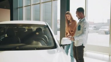 Modern otomobil merkezinde yürürken Afrikalı Amerikalı erkek ve beyaz kadın. Araba galerisinde yürüyen güzel bir çift. Satın almak için bir araç seçen arabalara bakıyor.