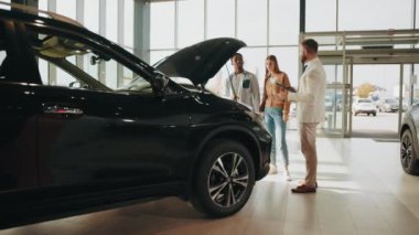 Afrikalı bir adam ve beyaz bir kadın galeride araba seçerken işinin ehli bir satıcıyla konuşuyor. Pahalı alışverişte çift birlikte seçim yapıyor. Araba satıcısı çalışıyor. Çeviri: teşekkür ederim.