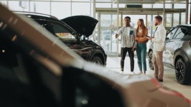 Yetenekli araba satıcısı müşterileriyle çalışmak için dijital tablet kullanıyor. Satış merkezinden araba alırken çok ırklı bir çift müdürle konuşuyor. Çeviri: teşekkür ederim.