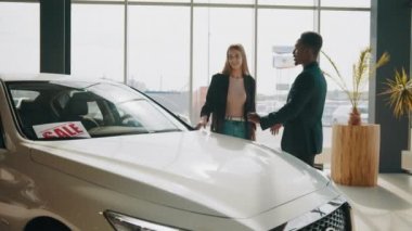 Afrikalı erkek ve beyaz kadın galeride yeni bir araç seçiyor. Araba seçen bir çift, kadın ve erkek galeride çeşitli arabalara bakıyor. Araba alıcıları. Galerideki Araç Satın Alma Merkezi