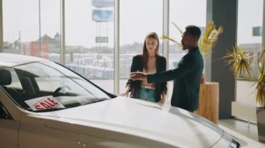 Afrikalı erkek ve beyaz kadın galeride yeni bir araç seçiyor. Satış merkezindeki araç satın alma. Birkaç araba galeride arabaya bakıyor. Otomobil bayilik merkezinde lüks otomobil.