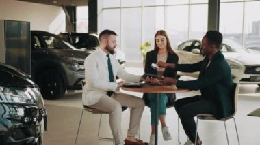 Mutlu Afro-Amerikalı adam kredi kartını ödeme için kullanıyor ve galeride beyaz kadınıyla yeni bir araba alıyor. Satıcı, kuaförde çok ırklı müşterilerle çalışıyor. Yeni araba alınıyor