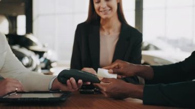 Mutlu Afrikalı Amerikalı adam yeni araba alırken kredi kartını kullanıyor. Çok ırklı bir çift oto galeride satış elemanı ile oturuyor ve araba satın almayla ilgili sözleşme imzalıyor. Yeni araba