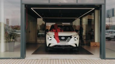 Modern oto kuaföründen çıkan büyük kırmızı yayı olan yeni beyaz lüks bir araba. Pahalı bir alıcı. Ulaşım, sürpriz ve satış kavramı. Modern salonda büyük kırmızı fiyonklu yeni beyaz lüks araba.