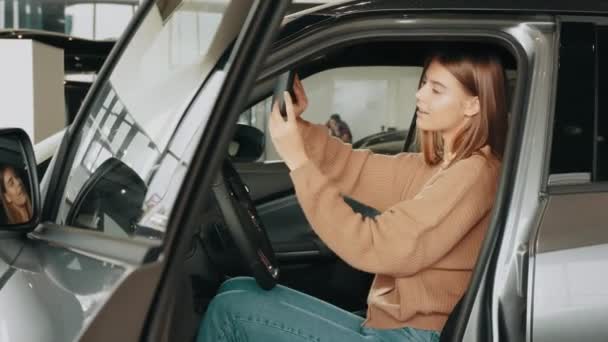 Zbliżenie szczęśliwej brunetki testującej samochód od wewnątrz podczas wizyty w salonie samochodowym. Biała kobieta testuje auto przed dokonaniem zakupu. Pojęcie ludzi i transportu, samochód — Wideo stockowe