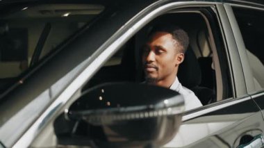 Lüks arabasında elinde anahtarlarla oturan bir adam. Yakışıklı adam başarılı bir alımdan memnun görünüyor. Yeni arabasında oturan ve anahtarlarını pencereden gösteren bir adam..