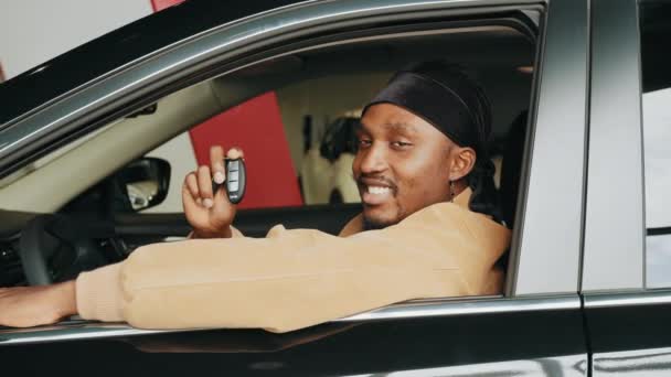 Homem africano animado mostrando uma chave de carro dentro de seu novo veículo. A visitar a concessionária de carros. Carro próprio. alegre afro-americano cara segurando auto chave no automóvel no negócio loja sentado no novo carro — Vídeo de Stock