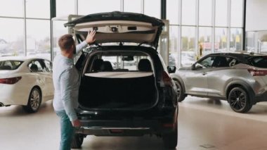 Yakışıklı adam pahalı siyah bir otomobilin bagajını açıyor. Genç müşteri alacağı arabanın bagajını kontrol ediyor. Modern bir galeride arabanın bagajını açıyorum. Arabaya bakıyorum..