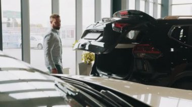 Modern bir galeride arabanın bagajını açıyorum. Yakışıklı adam pahalı siyah bir otomobilin bagajını açıyor. Genç müşteri alacağı arabanın bagajını kontrol ediyor. Arabaya bakıyorum..