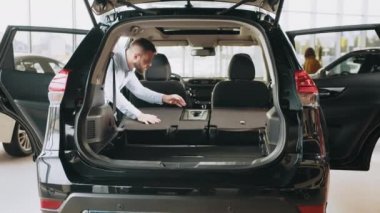 Adam galeride araç seçiyor. Sakallı genç adam arabaya dikkatlice bakıyor. Adam arabanın işlevlerini ve pratiğini kontrol ediyor. Katlanan koltuklar ve yeni bir arabanın bagajı.