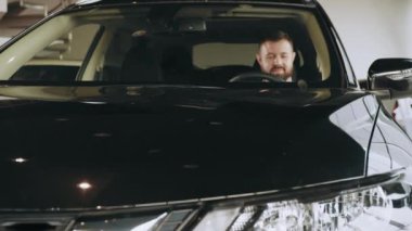 Yeni arabanın içinde oturan mutlu beyaz adam ve galeride yeni modelin tüm fonksiyonlarını kontrol ediyor. Modern kuaförde çeşitli otomobilleri inceleyen erkek müşteri. Modern galeride arabayı inceleyen adam.