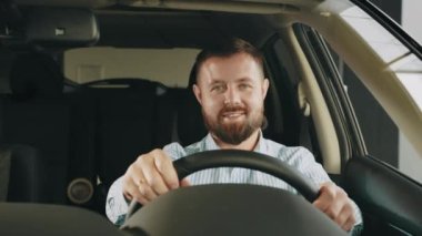 Yeni arabasında oturan mutlu, gülümseyen genç bir alıcı bayi otoparkının dışında izole edilmiş geziye hazır bekliyor. Araba galerisindeki arabaya bakan bir adam. Otomatik satın alma kavramı