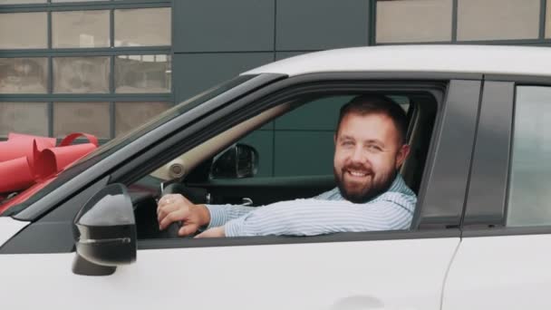 Hombre sonriente sentado en coche moderno blanco después de la prueba de manejo. Feliz cliente masculino comprando auto nuevo en el centro de concesionarios. Concepto de compra y venta caro. Hombre tomando un coche nuevo para la prueba de manejo — Vídeos de Stock