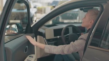 Eko araba satışı konsepti. Otomatik sürüş sistemi olan yeni nesil elektrikli aracın test sürüşü. Çekici beyaz kadın yeni modern arabanın direksiyonunda oturuyor ve kameraya gülümsüyor..